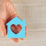 'hand holding a cutout shaped like a house with a heart in it'