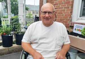 Resident Carl Barna smiling next to a thriving garden
